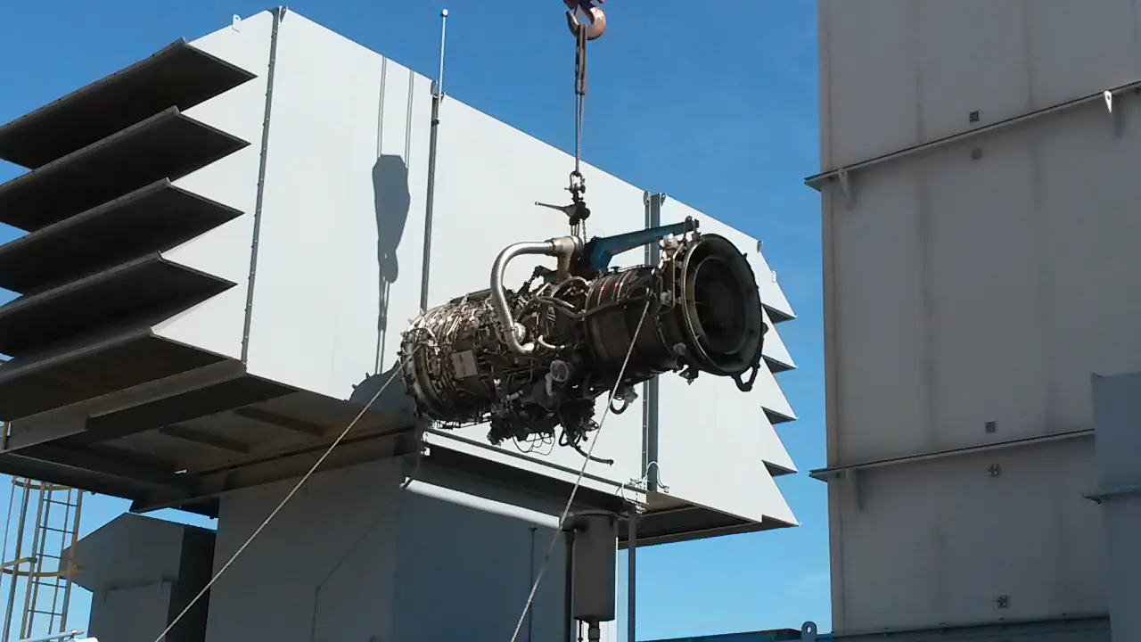 A crane is lifting an engine from the ground.